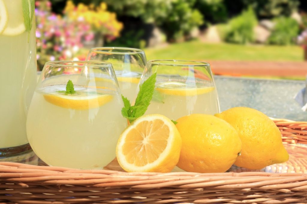 Lemoniada cytrynowa w szklankach i cytryny na stoliku ogrodowym - Przepisy na orzeźwiające lemoniady