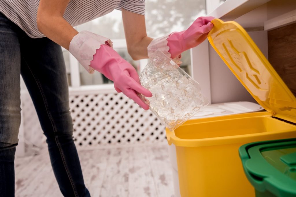 Kobieta wyrzucająca do żółtego śmietnika plastikowe opakowanie – segregowanie śmieci – Jak ograniczyć odpady w codziennym życiu?