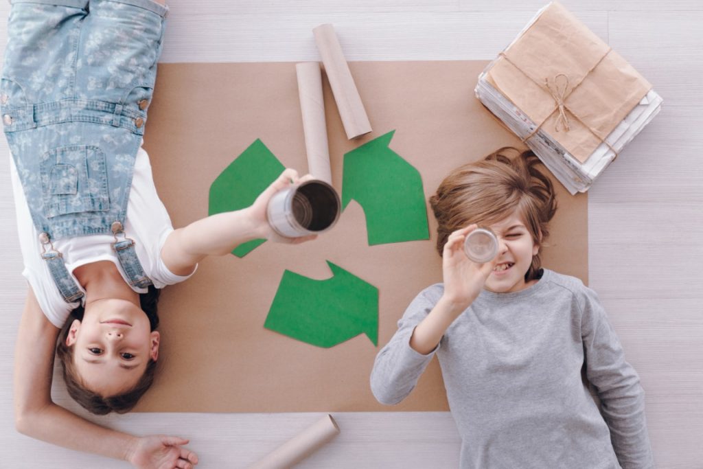 Chłopiec i dziewczynka leżący na podłodze i bawiący się papierem z recyklingu
