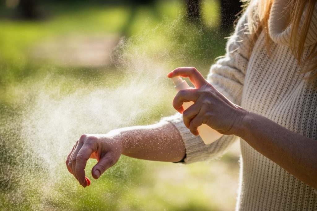 Kobieta pryskająca rękę sprejem na komary – Co zabrać ze sobą na wycieczkę do lasu? - Velvet