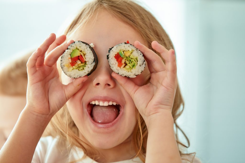 Dziewczynka z dwoma kawałkami sushi przy twarzy