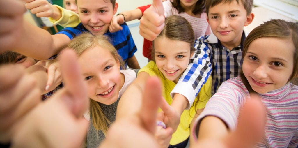 Grupa uśmiechniętych dzieci z wyciągniętymi kciukami w górę wskazującymi znak OK