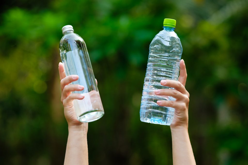 Dłonie trzymające szklaną i plastikową butelkę