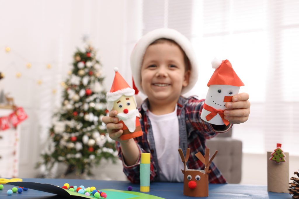 Uśmiechnięty chłopiec pokazujący własnoręcznie zrobione Mikołaje z rolek po papierze toaletowym