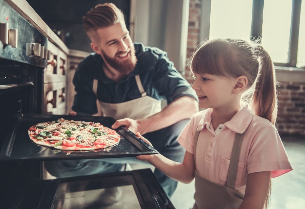 Międzynarodowy Dzień Pizzy – tata i córka wkładają do piekarnika domową pizze